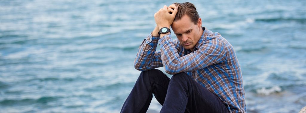 man thinking on rock by water